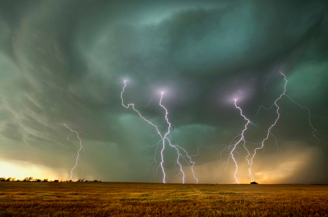 Green and black clouds. Multiple lightning bolts strike the ground over the Great Plains.