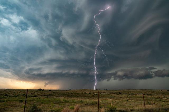 A single lightning bolt hits the ground in front of a supercell over the prairie.