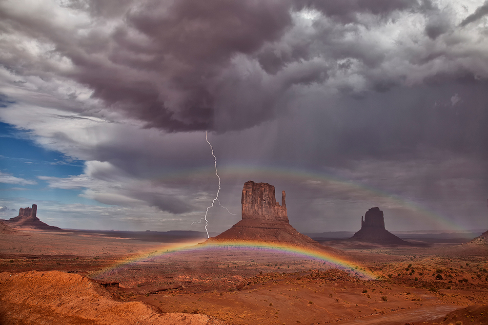 A storm over Monument Valley with a lightning bolt and a double rainbow